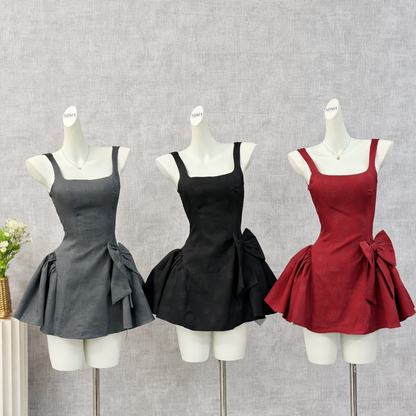 Display of three mini dresses on mannequins in gray, black, and burgundy colors, each with bow detail and flared skirt on neutral background