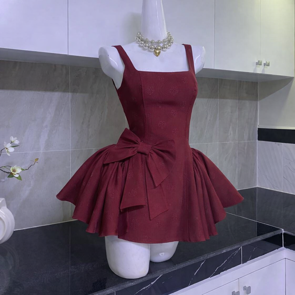 Mannequin showcasing burgundy mini dress with wide straps, square neckline, flared skirt, and large bow on side in tiled kitchen setting