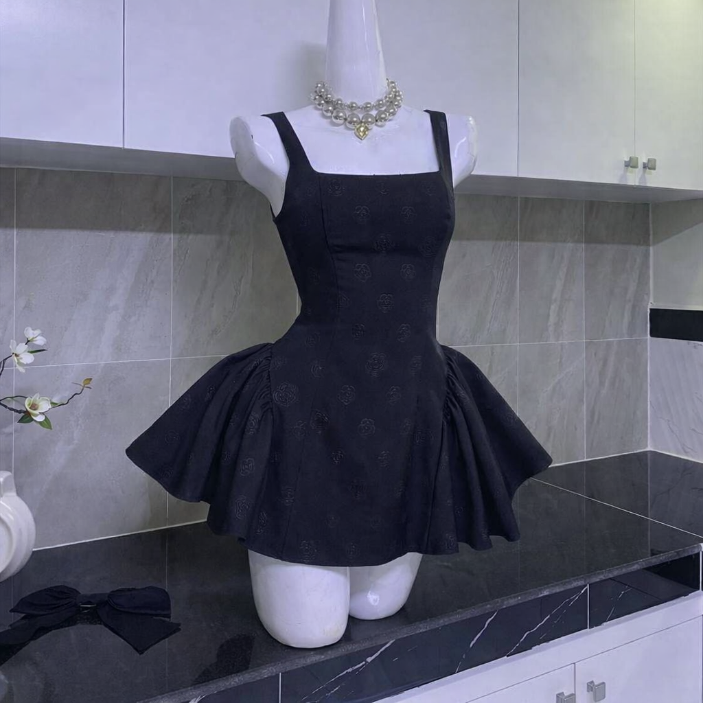 Mannequin wearing black mini dress with square neckline, thick straps, flared skirt, and large black bow on side in kitchen