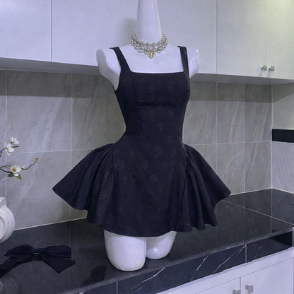 Mannequin wearing black mini dress with square neckline, thick straps, flared skirt, and large black bow on side in kitchen