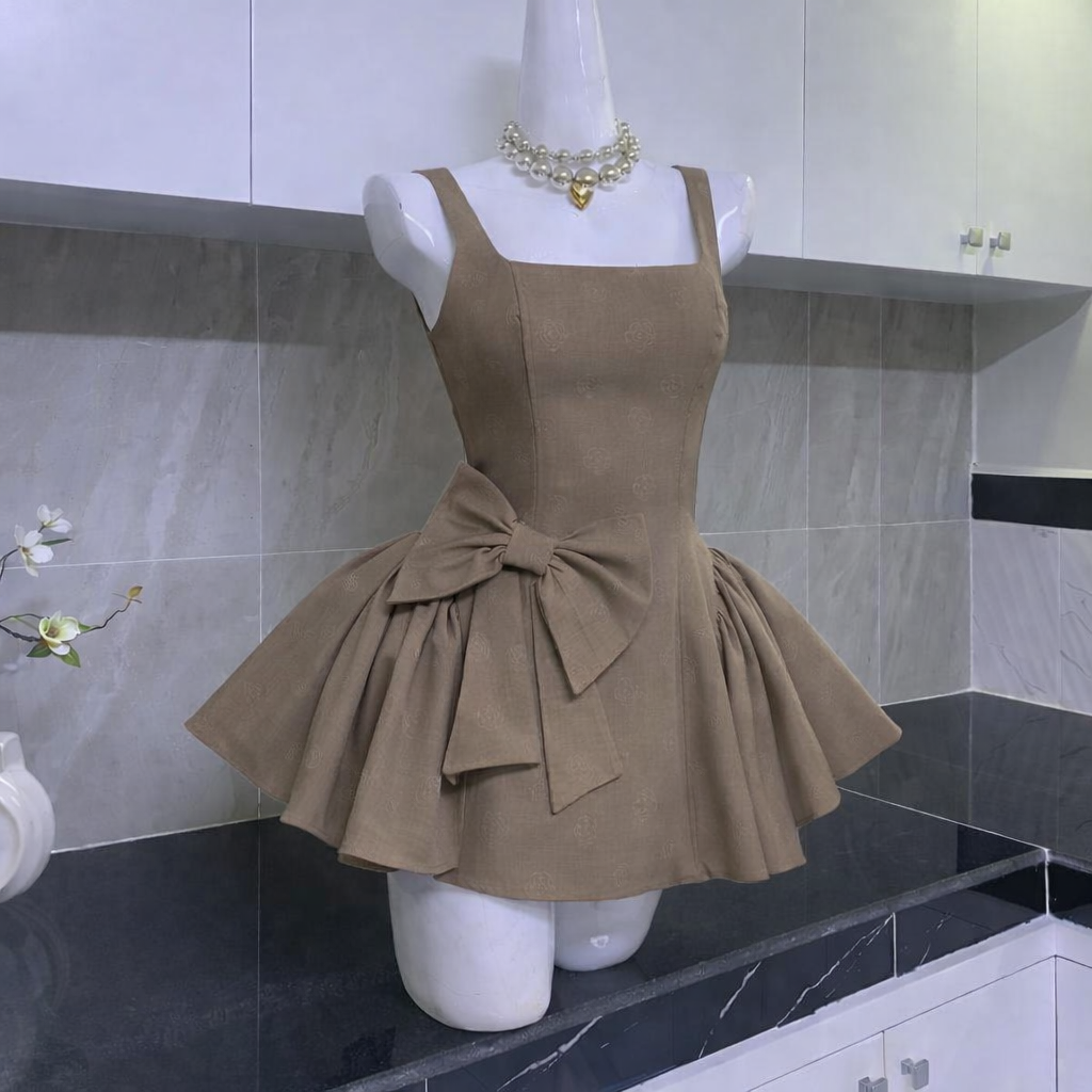 Mannequin dressed in taupe mini dress with square neckline, flared skirt, and oversized bow detail in kitchen environment