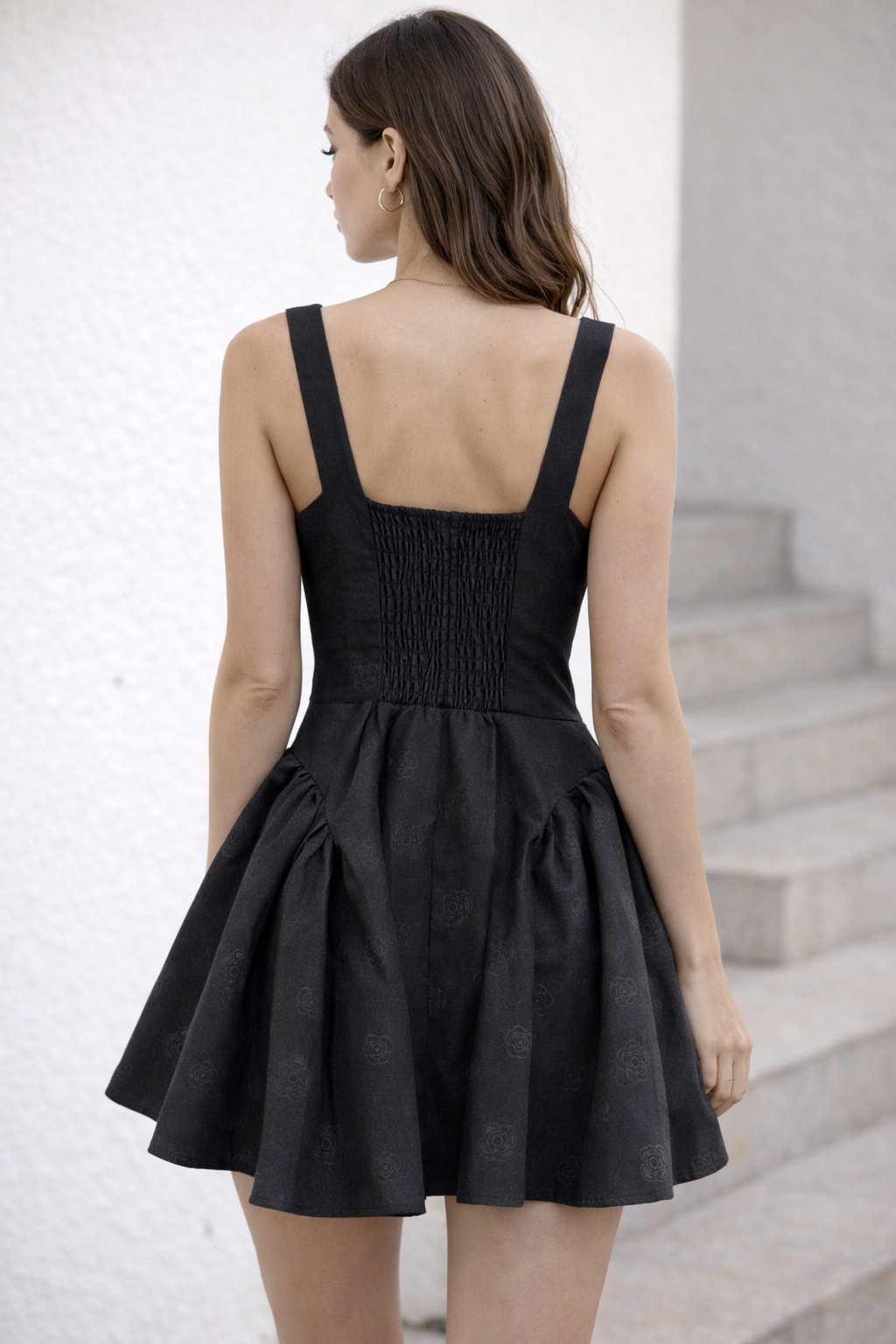 Rear view of female model in black mini dress with elastic shirring and flared skirt outdoors