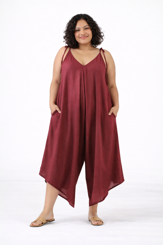 Plus size woman modeling burgundy flowy wide-leg jumpsuit with adjustable shoulder ties and pockets