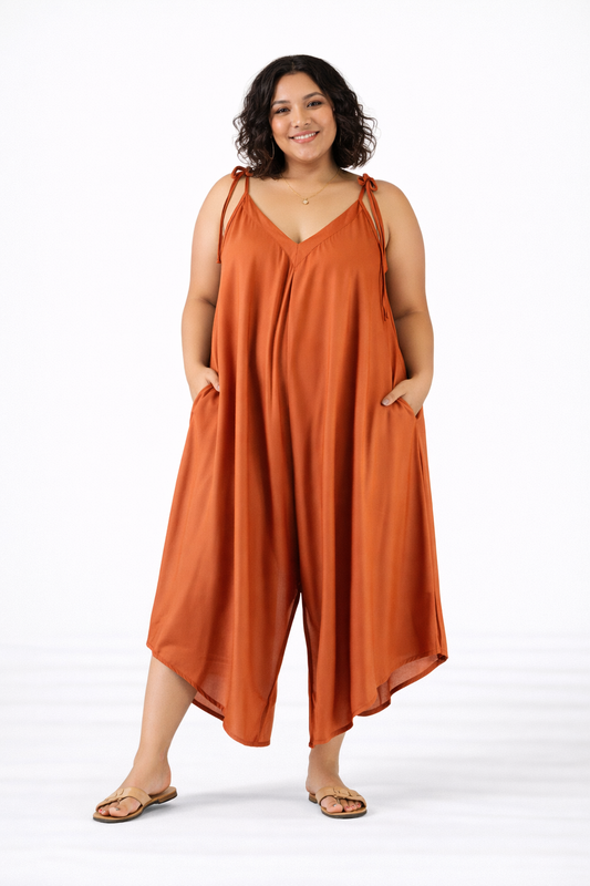 Plus size woman showcasing burnt orange jumpsuit with loose fit and tie shoulder straps